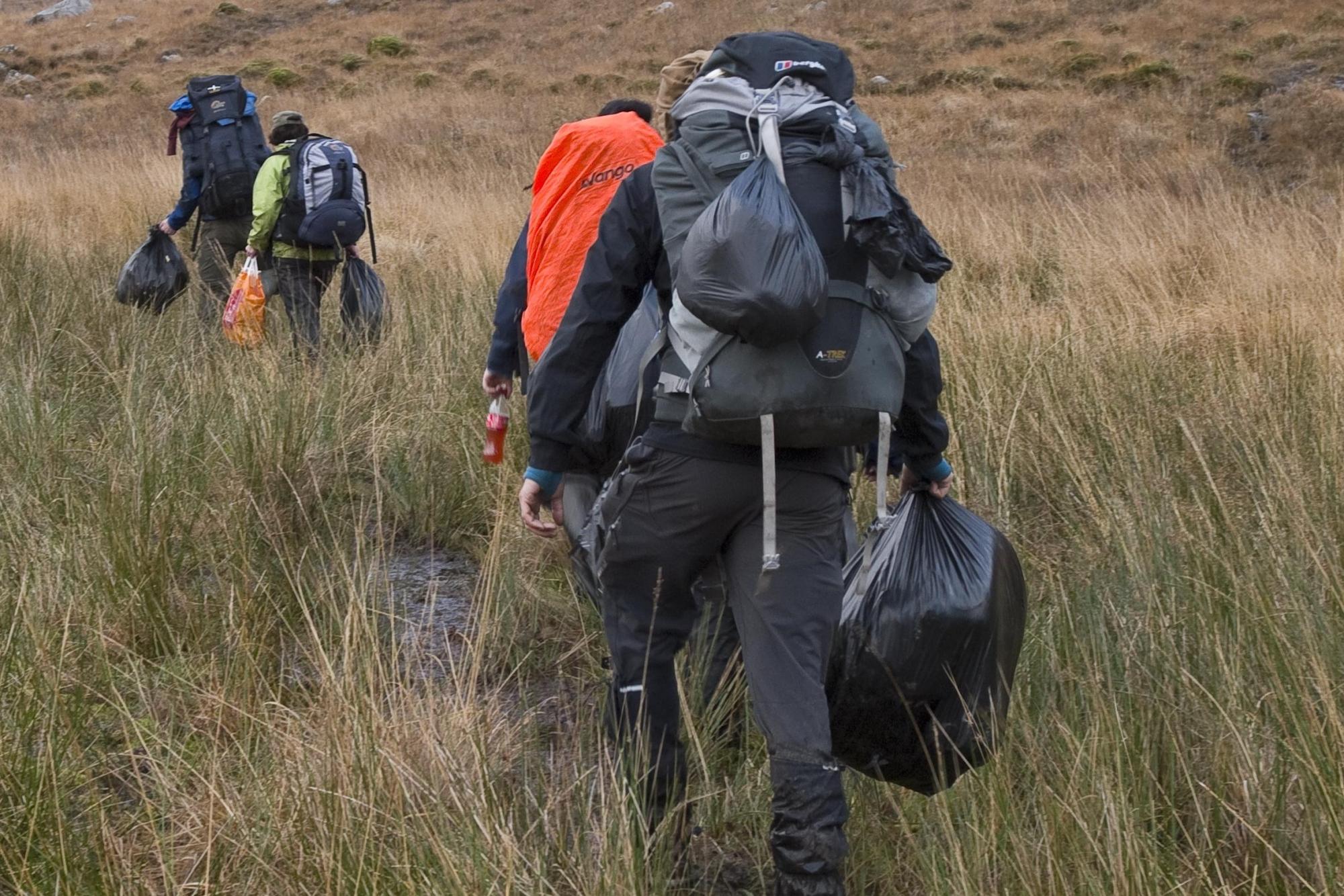 A group of people walking, wearing rucksacks and carrying full black bin liners